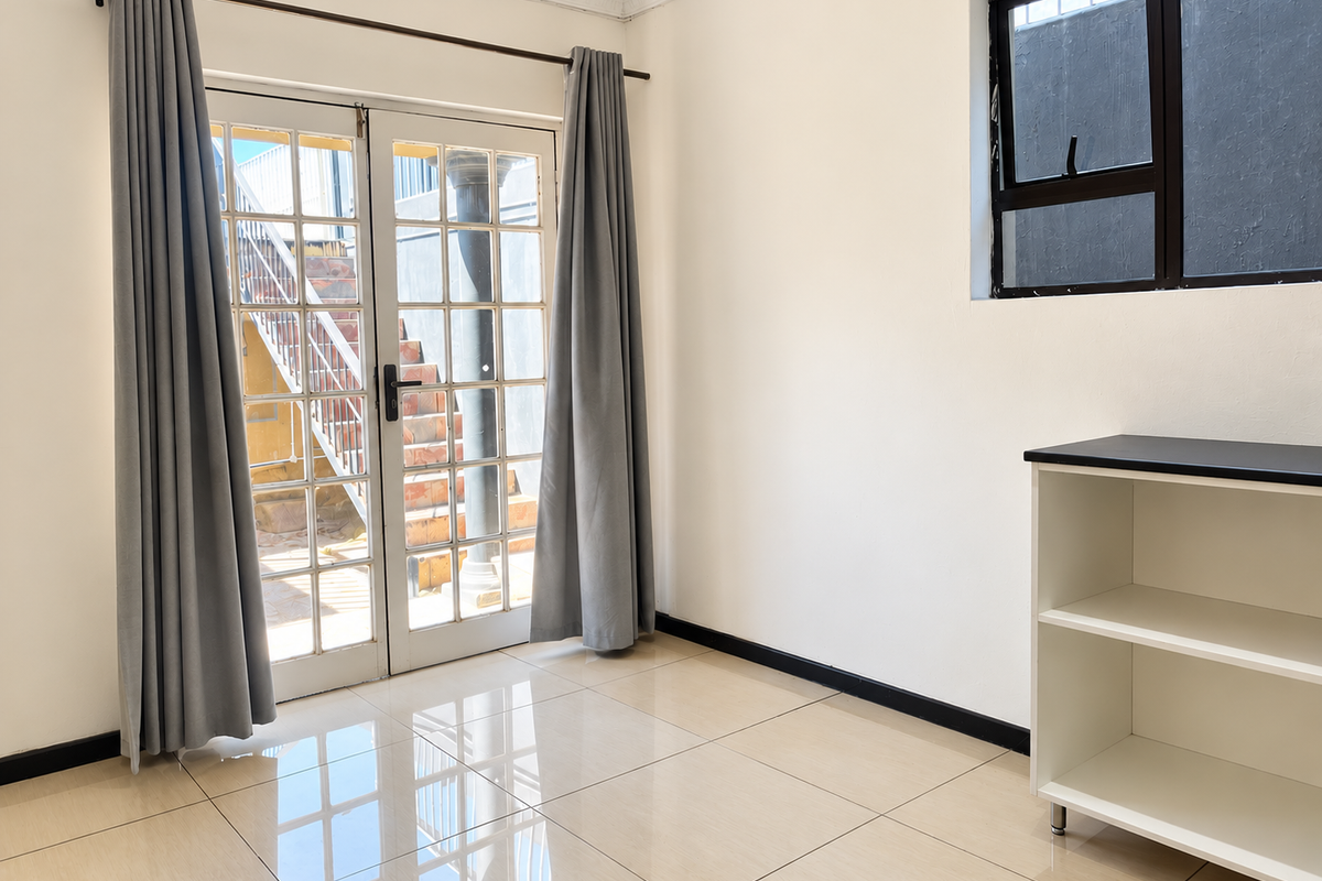 A bright, empty living area featuring polished tiled floors, a large window, and French doors providing access to an outdoor staircase.