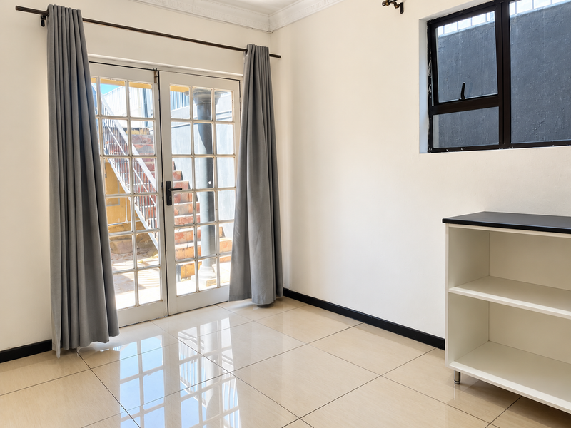 A bright, empty living area featuring polished tiled floors, a large window, and French doors providing access to an outdoor staircase.