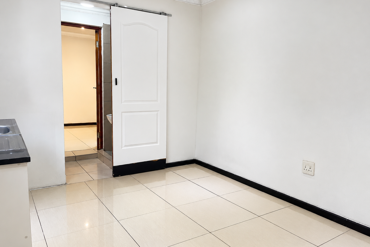 An empty open-plan living area featuring tiled flooring, a sliding door, and a partial view of an adjacent room.