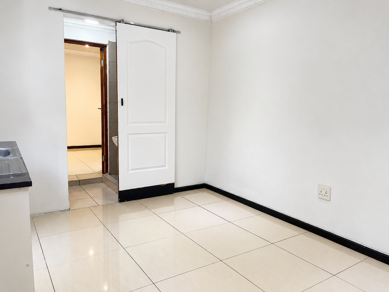 An empty open-plan living area featuring tiled flooring, a sliding door, and a partial view of an adjacent room.