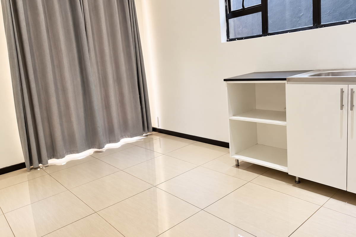 A clean, modern kitchen area featuring tiled flooring, white cabinetry with a black countertop, a stainless steel sink, and large windows.