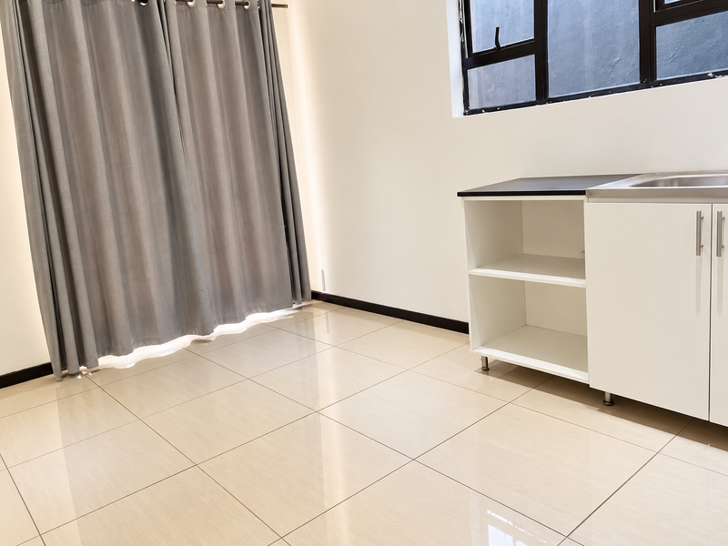 A clean, modern kitchen area featuring tiled flooring, white cabinetry with a black countertop, a stainless steel sink, and large windows.