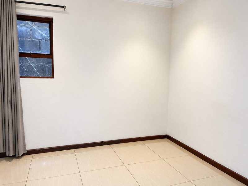 A clean, empty bedroom featuring neutral tiled flooring, timber skirting boards, and a timber-framed window, providing a blank canvas for personalization.