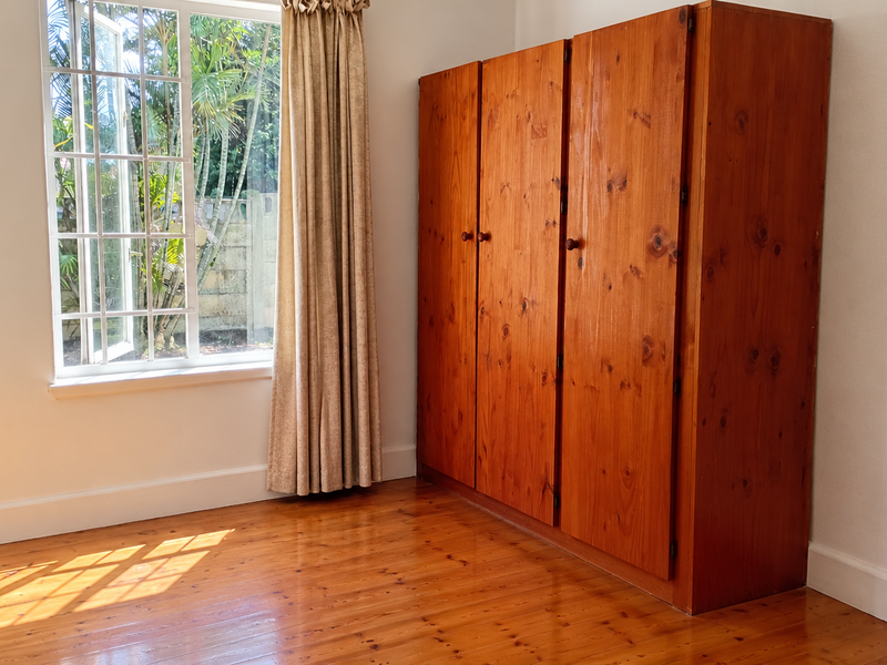 A bedroom featuring polished timber flooring, a large casement window providing natural light, and built-in wooden cabinetry.