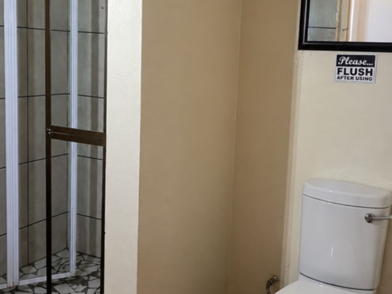 A functional bathroom featuring a shower enclosure with tiled walls and a standard toilet, requiring some cosmetic updates to improve its overall condition.
