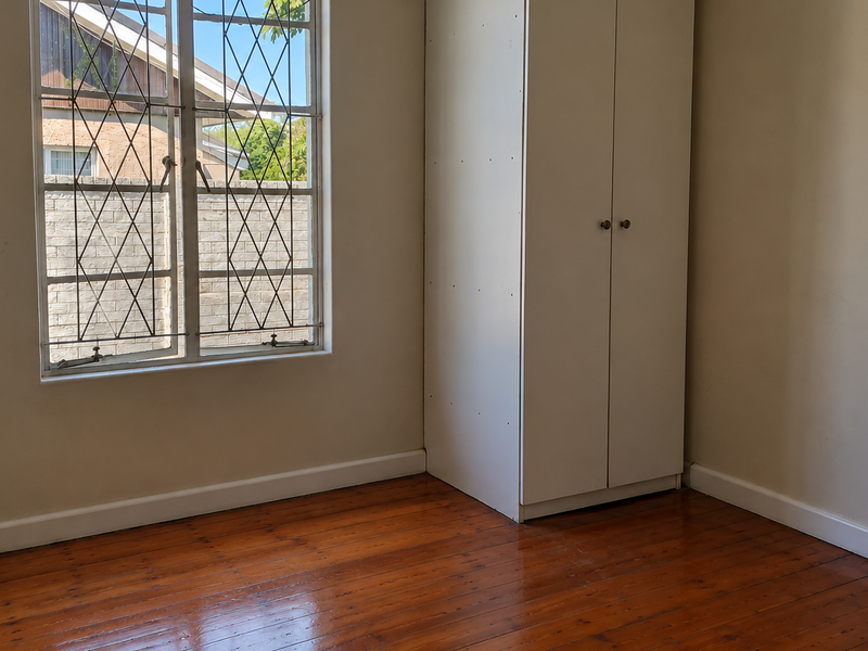 A vacant bedroom featuring polished timber flooring, a built-in wardrobe, and a window with security bars.