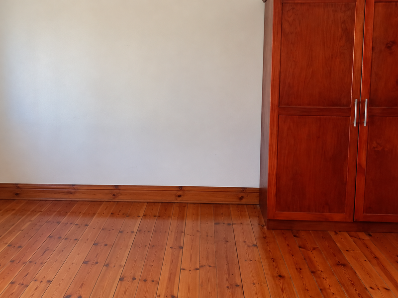 A clean bedroom featuring polished timber flooring, matching timber skirting boards, and a built-in wooden wardrobe.