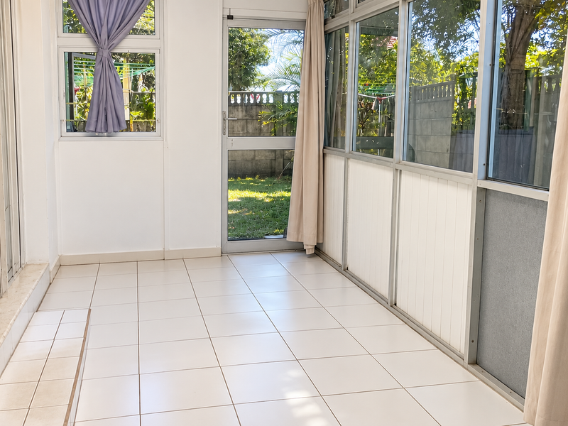 A bright, enclosed patio area featuring tiled flooring and extensive aluminium-framed glass windows and doors, offering a clear view of the garden.