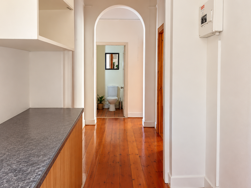A bright hallway featuring polished timber flooring, an elegant arched transition, and built-in cabinetry, leading towards a bathroom.