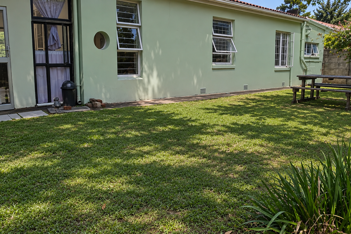 A view of the rear exterior of the house featuring a green facade, multiple windows, and a well-maintained lawn area.