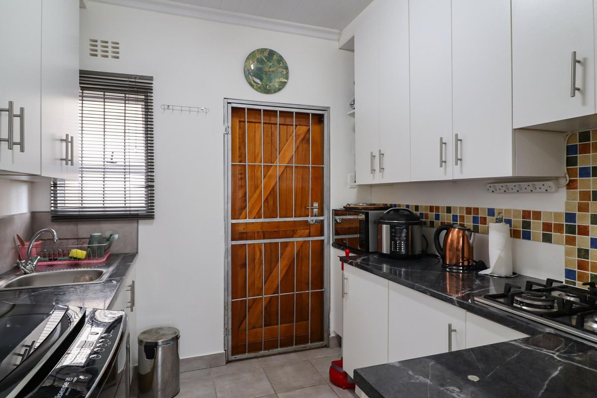 A functional kitchen featuring white cabinetry, dark stone-look countertops, a built-in gas hob, and a secure wooden door with a metal security gate.