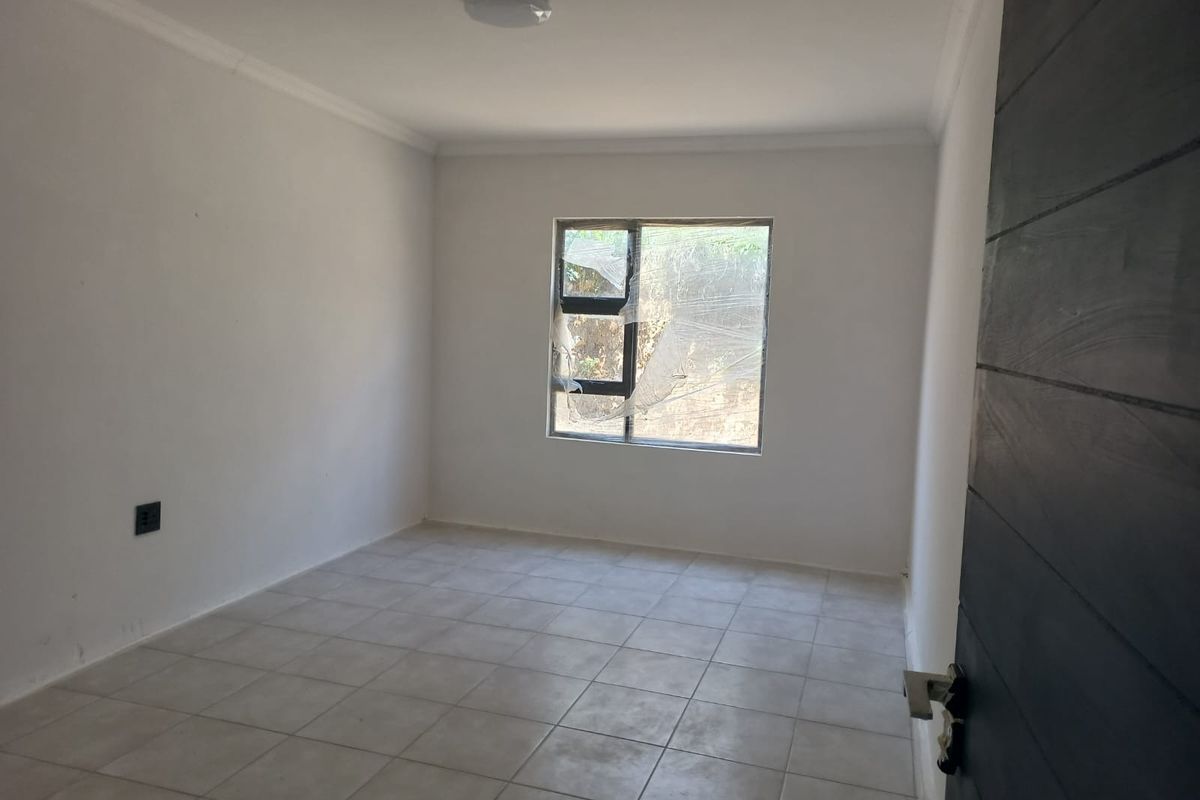 An empty bedroom featuring tiled flooring, a ceiling light fixture, and a window with damaged protective film.