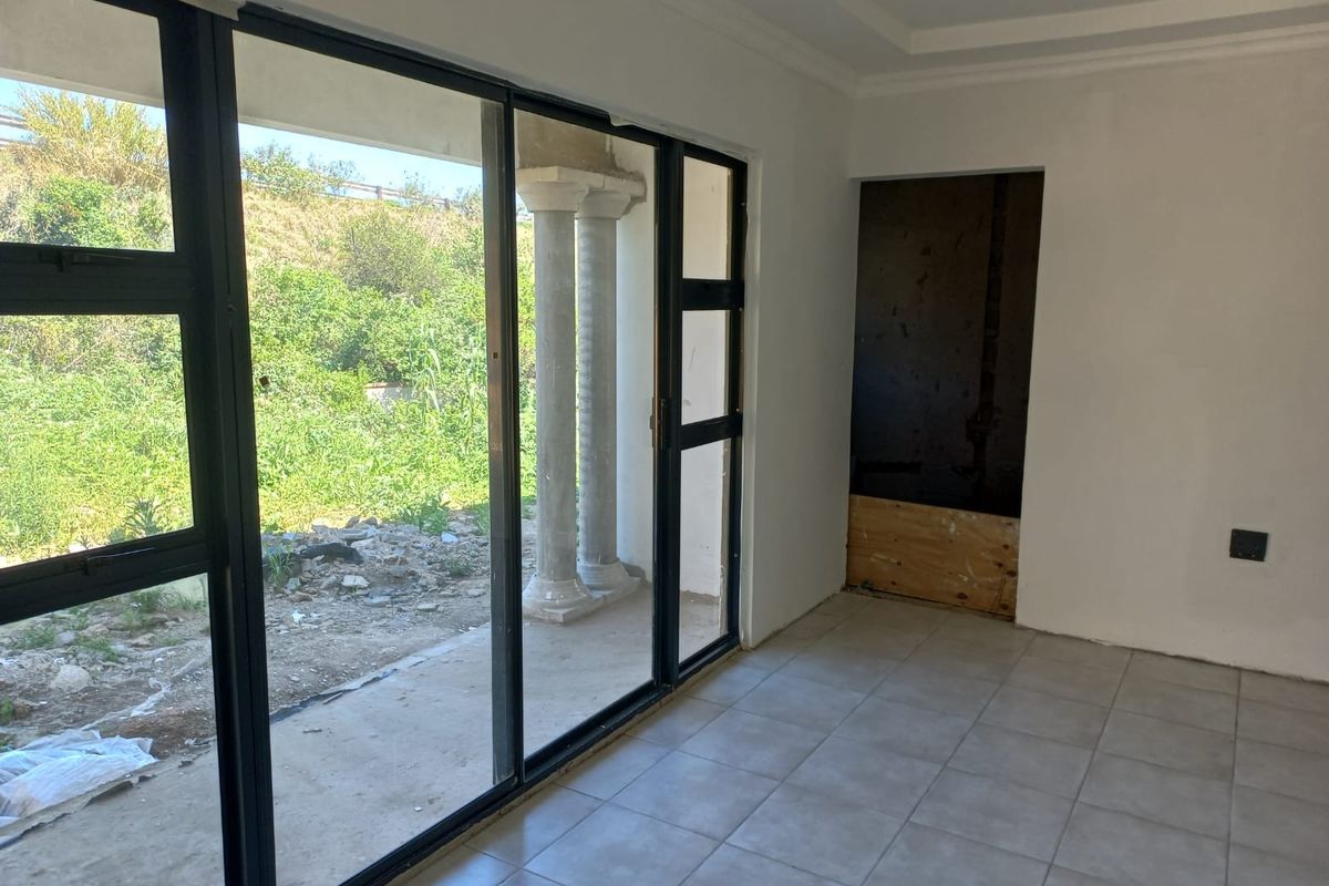 An interior living space featuring large black-framed sliding glass doors leading to an outdoor area with decorative columns and unfinished garden space.