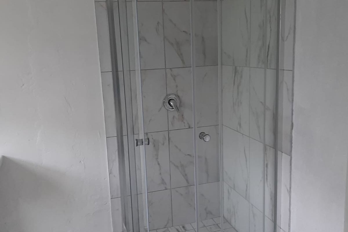 A modern shower enclosure featuring marble-look wall tiles and a glass door, set within a neutral bathroom space.