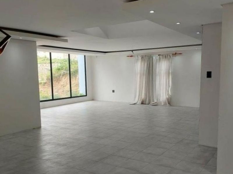 Spacious open-plan living area featuring large windows, recessed ceiling lighting, and neutral tiled flooring, offering a bright and versatile space.