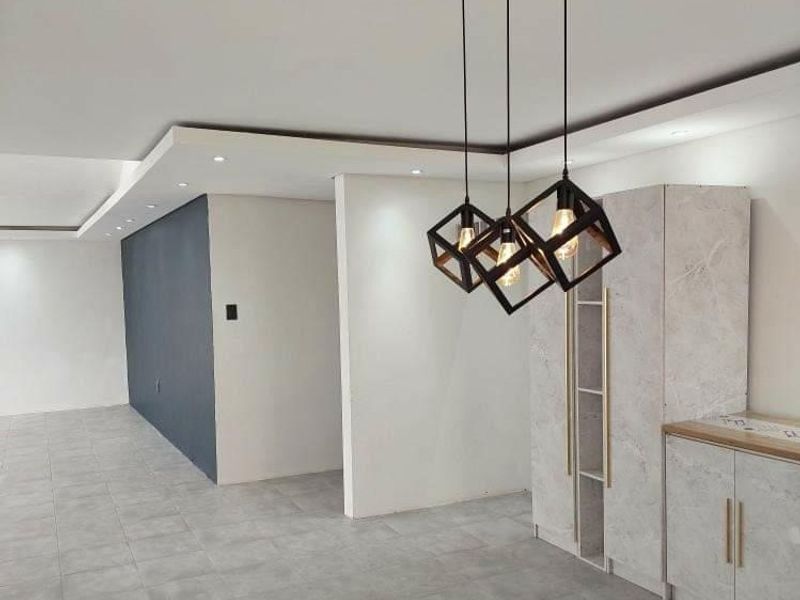 Modern open plan living area featuring recessed ceiling lighting, contemporary pendant light fixtures, and built-in cabinetry with a marble-effect finish.