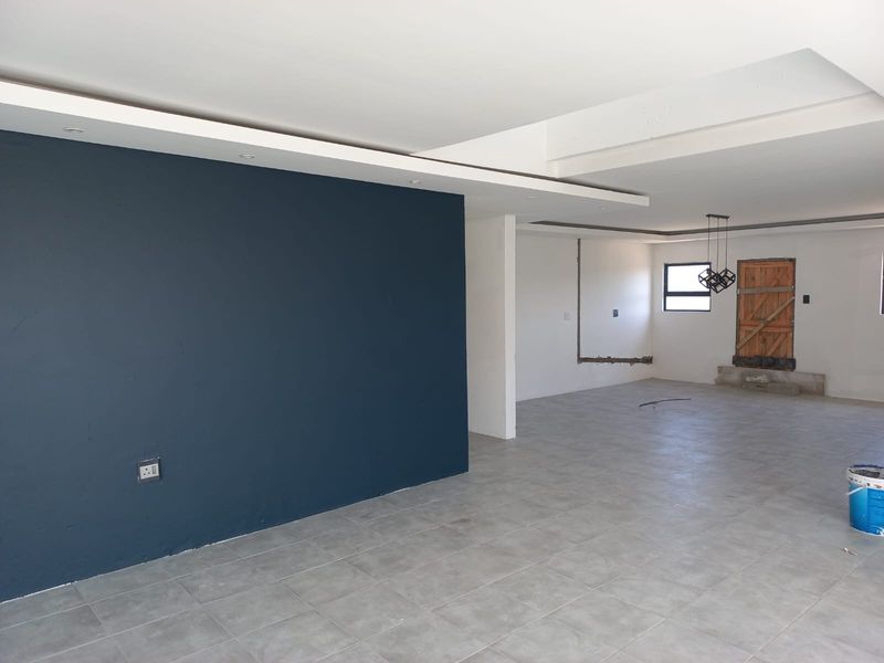 An open-plan living area featuring large format floor tiles, a dark accent wall, and recessed ceiling details, currently undergoing renovation.