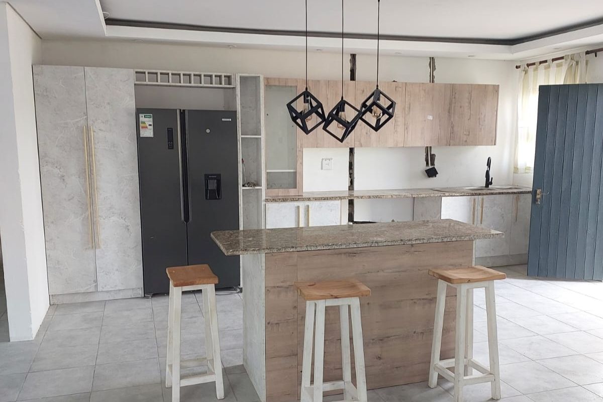 Modern kitchen featuring a central island, stone countertops, wood-look cabinetry, and contemporary pendant lighting, with tiled flooring throughout.