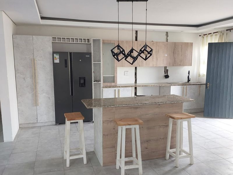 Modern kitchen featuring a central island, stone countertops, wood-look cabinetry, and contemporary pendant lighting, with tiled flooring throughout.