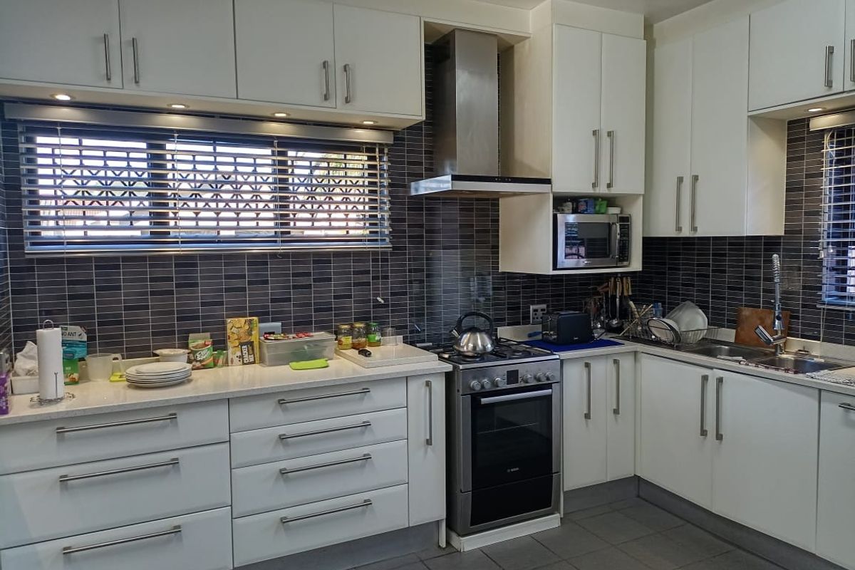 Modern kitchen featuring white cabinetry, stone countertops, stainless steel oven with extractor fan, and dark tiled backsplash.