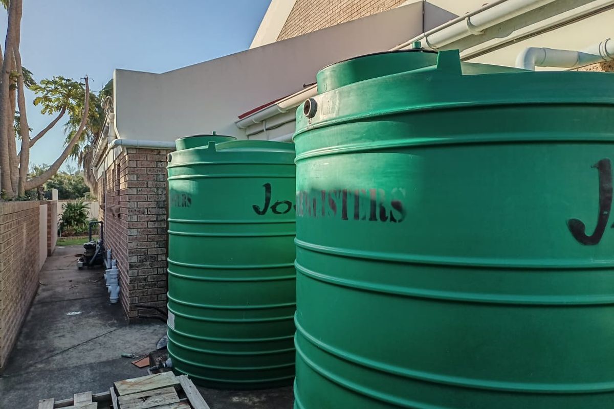 Side exterior area featuring two large green water storage tanks connected to the building's guttering system.