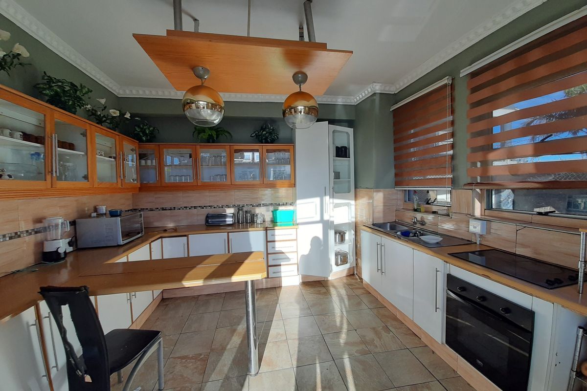A functional kitchen featuring wooden upper cabinetry, white lower cabinets, a built-in oven, hob, and a breakfast bar island with pendant lighting.