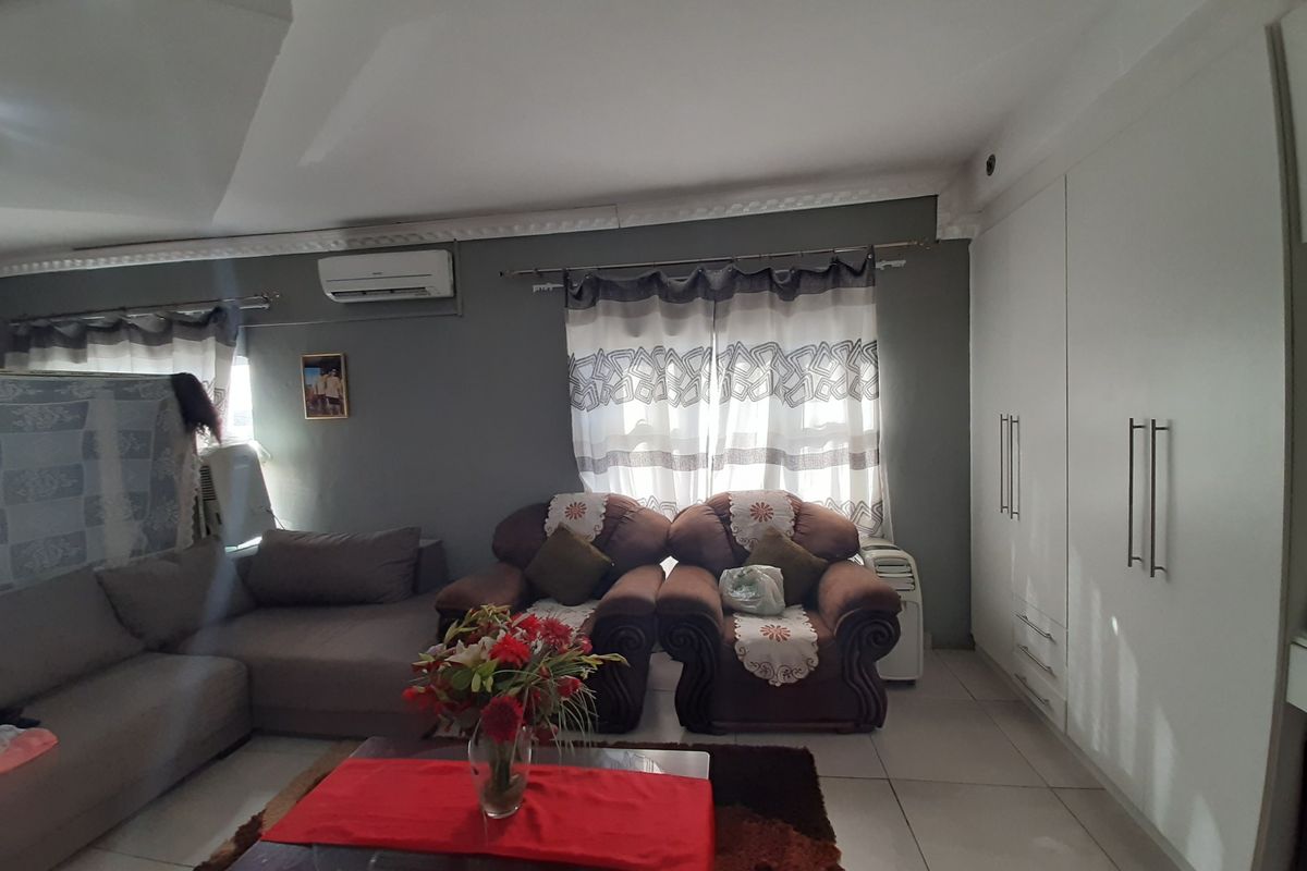 A living room featuring tiled flooring, built-in floor-to-ceiling cabinetry, and a wall-mounted air conditioning unit.
