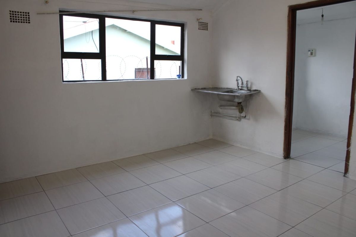A basic, empty kitchen area featuring tiled flooring, a single stainless steel sink, and a window with security bars.