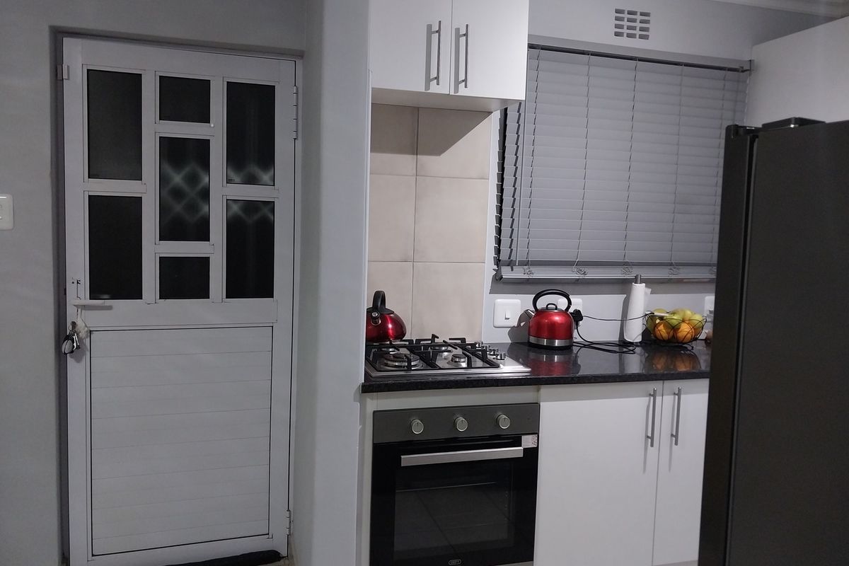 A compact kitchen area featuring a built-in oven, gas hob, white cabinetry, and a secure exterior door with glass panels.