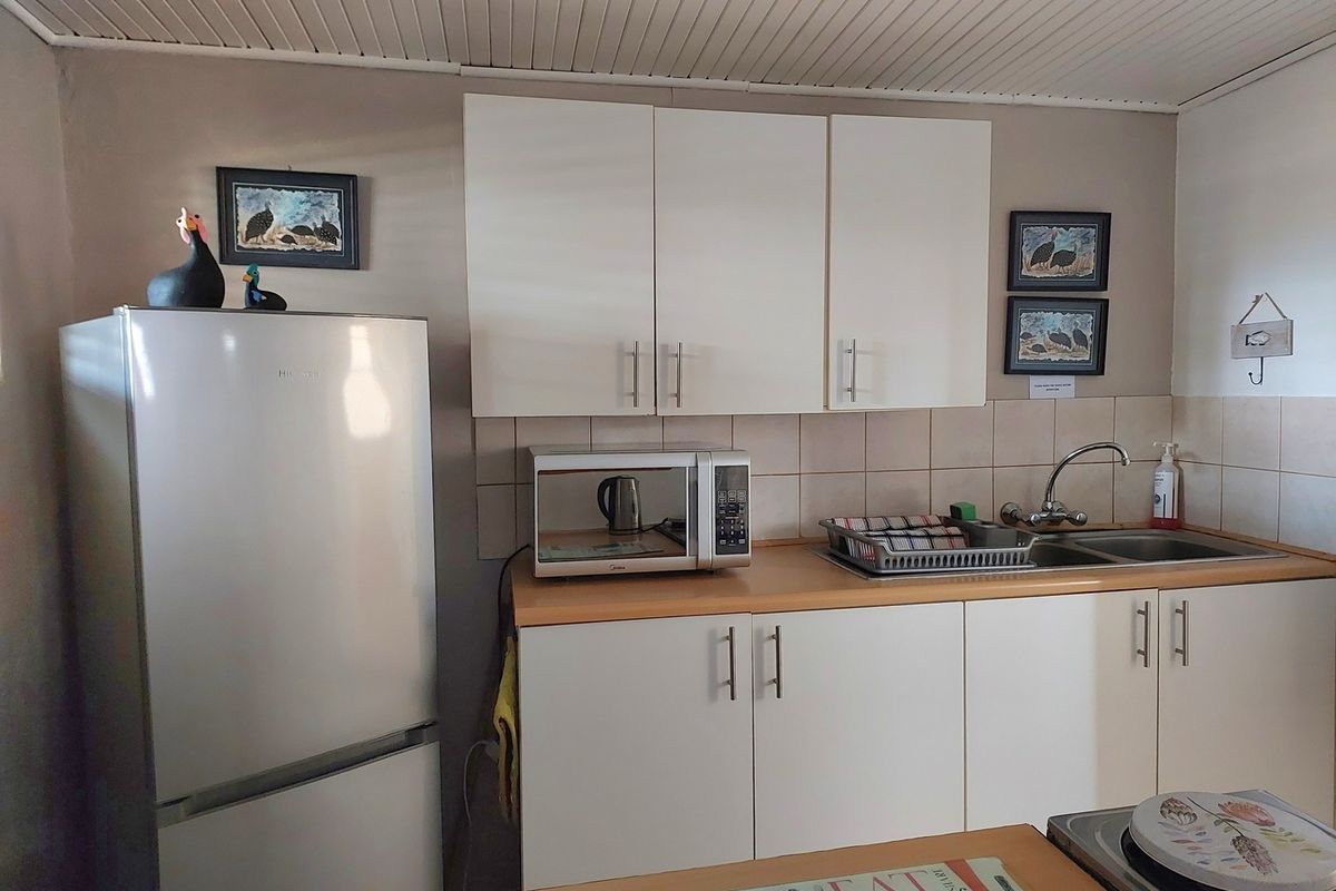 A functional kitchen featuring white cabinetry, light-toned countertops, a stainless steel sink, and tiled splashbacks.
