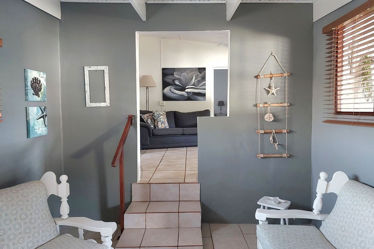 An interior view showing a split-level transition between rooms, featuring tiled flooring, a wooden handrail, and exposed beam ceiling details.