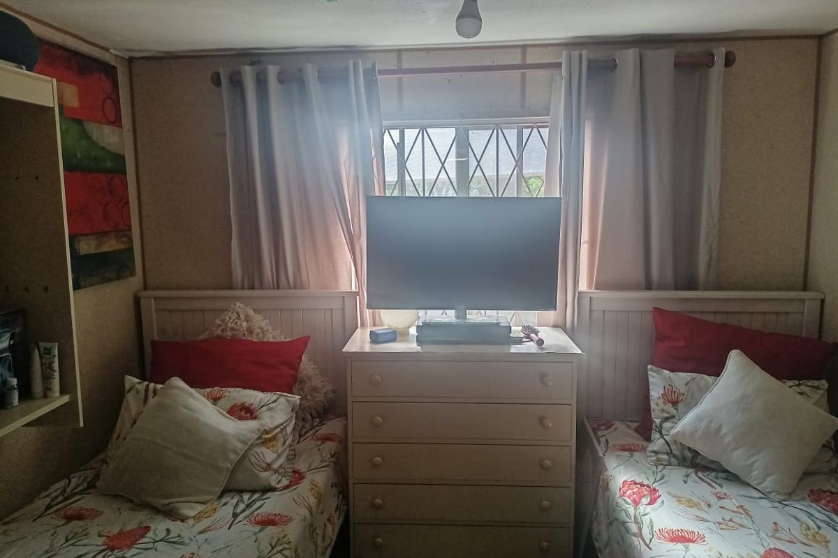 A bedroom featuring twin bed frames and a central dresser, with security bars on the window and basic ceiling lighting.