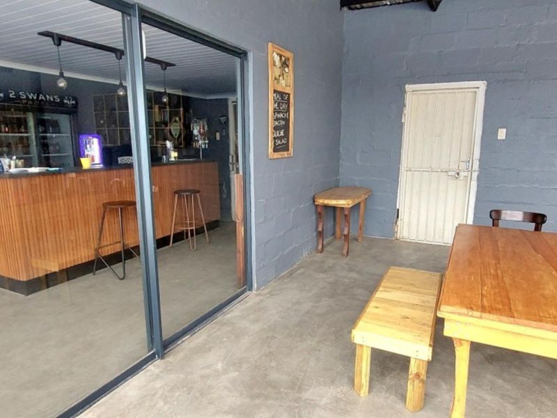 A covered patio area featuring concrete flooring, exposed blockwork walls, and a sliding glass door providing access to an indoor bar area.