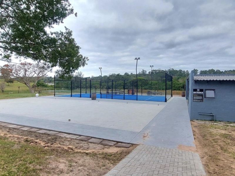 A well-maintained outdoor padel court facility featuring a paved patio area, perimeter fencing, and integrated floodlighting within a landscaped residential setting.