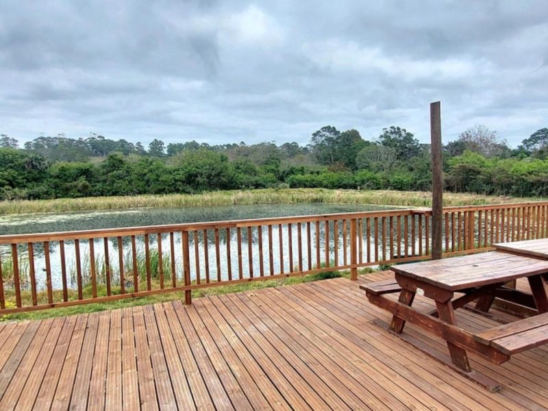 A spacious timber deck featuring a wooden balustrade, offering scenic views over a natural pond and surrounding greenery.