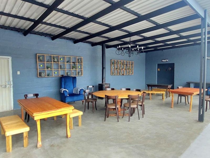 A spacious covered outdoor patio area featuring concrete flooring, exposed steel roof beams, and a wood-burning fireplace, suitable for events or social gatherings.