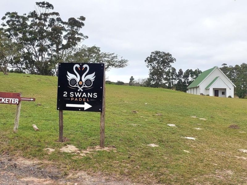 A view of the vacant residential land featuring directional signage and a distant building structure on the property.