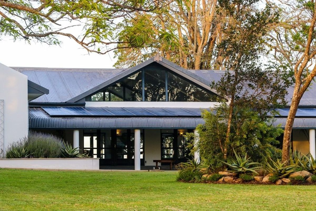 A view of the rear facade featuring a pitched roof, large triangular windows, and a covered patio area overlooking a landscaped garden.
