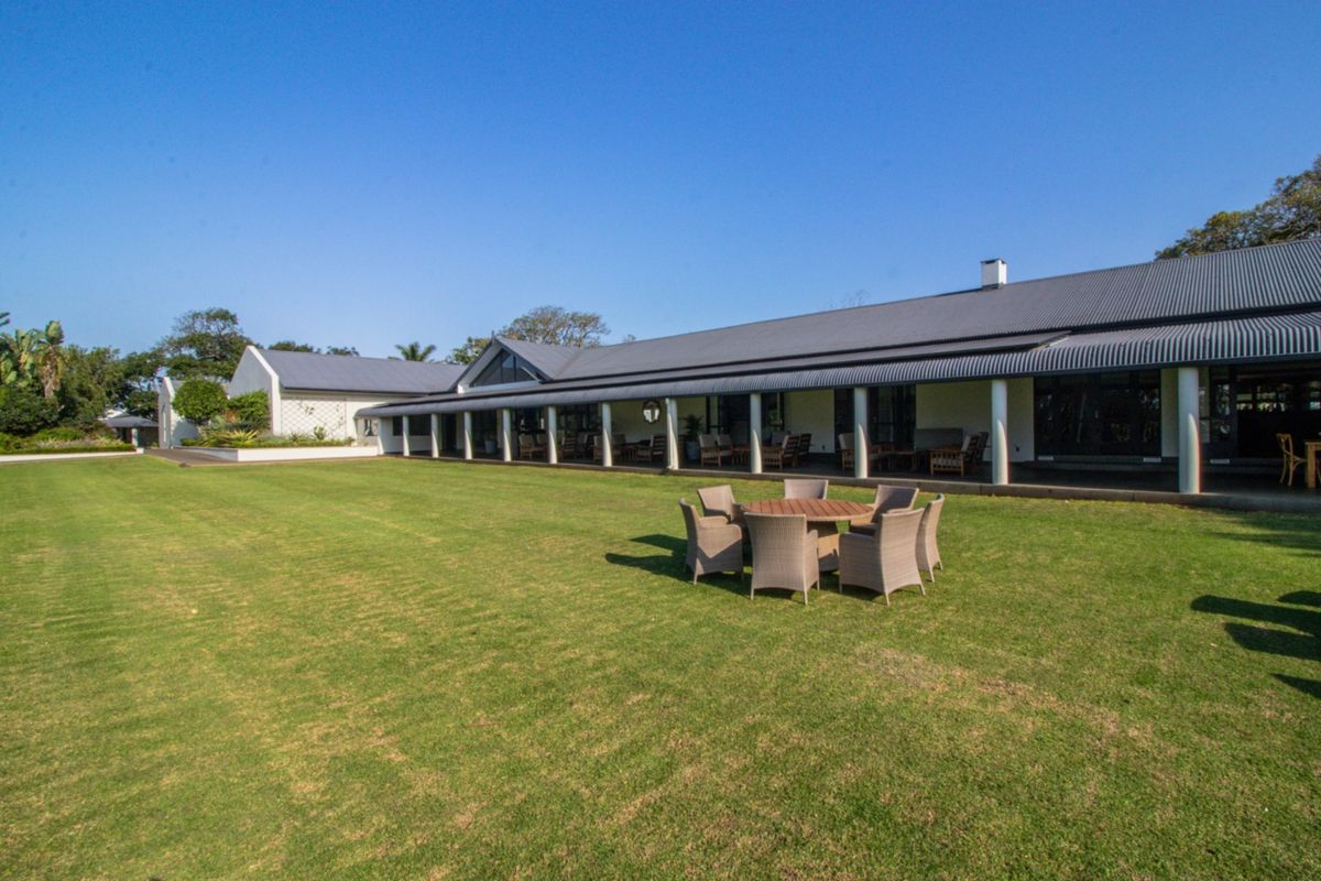 Spacious rear exterior view featuring a large manicured lawn and a long covered patio area with structural columns.