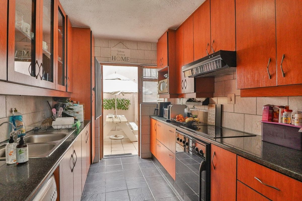 Galley-style kitchen featuring wood-veneer cabinetry, dark granite countertops, integrated hob and extractor fan, and direct access to an outdoor patio area.