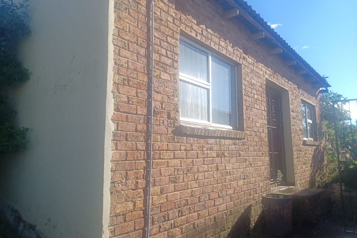 Exterior view of a single-story brick house featuring exposed face-brick walls, metal window frames, and a corrugated roof.
