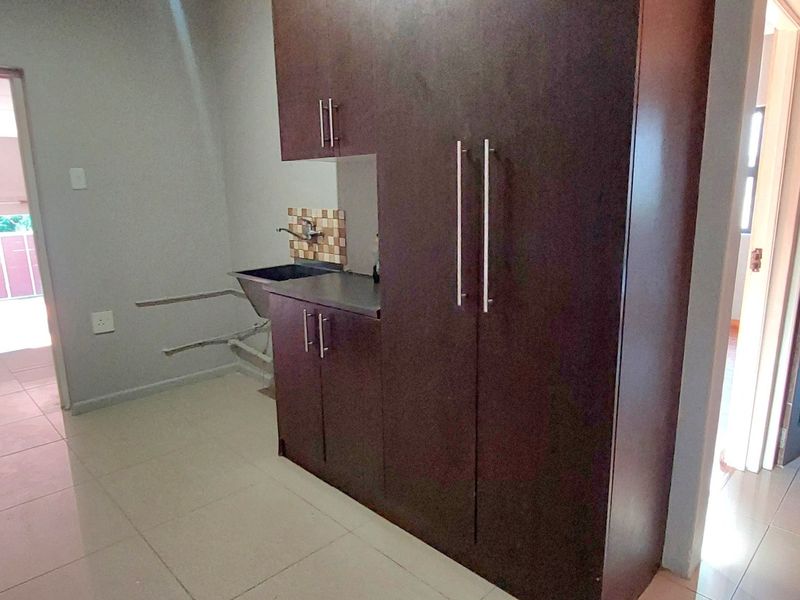 A functional scullery area featuring built-in dark wood cabinetry, a sink with a tiled splashback, and tiled flooring, providing additional utility space.
