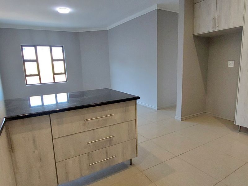 Modern kitchen featuring light wood-grain cabinetry, dark granite countertops, tiled flooring, and ample space for appliances in an open-plan layout.