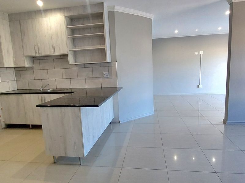 Spacious open-plan kitchen and living area featuring modern light-wood cabinetry, granite countertops, and neutral porcelain floor tiles throughout.