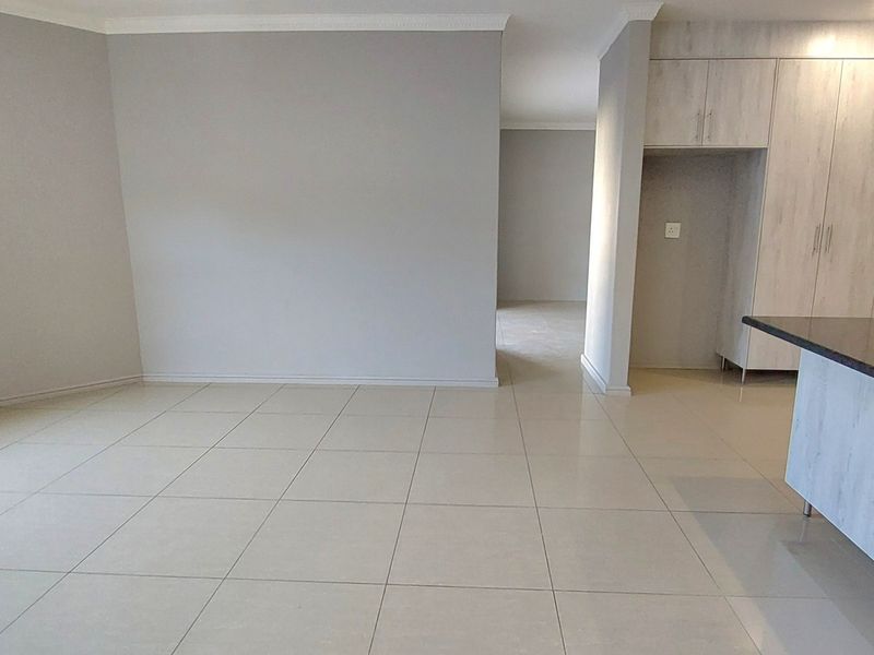 Spacious open-plan living area featuring neutral tiled flooring, modern built-in cabinetry, and a kitchen island with a stone countertop.