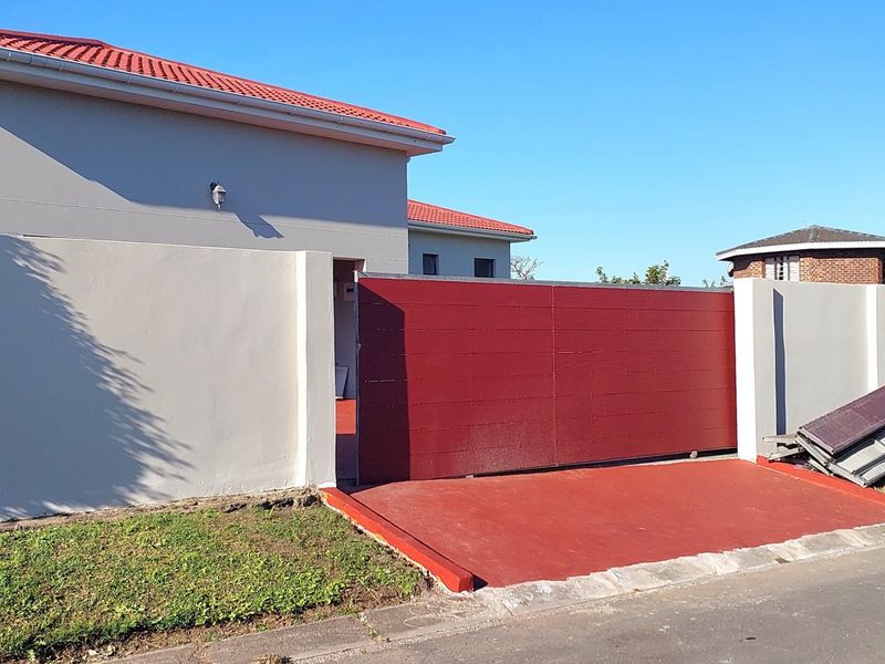 Front exterior view of the property featuring a red sliding gate, perimeter wall, and tiled roof structure.