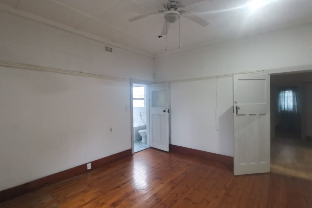 A spacious bedroom featuring polished timber flooring, a ceiling fan, and direct access to an adjoining bathroom.
