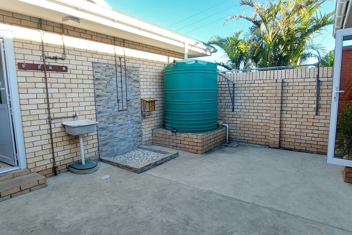 A functional rear courtyard area featuring a water storage tank, an outdoor shower with stone tiling, and a utility sink against a brick wall.