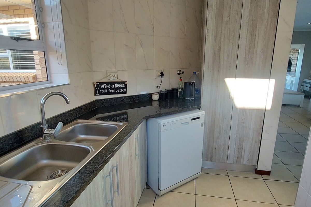 A functional kitchen area featuring granite countertops, a double stainless steel sink, tiled splashbacks, and built-in cabinetry with a dedicated space for a dishwasher.