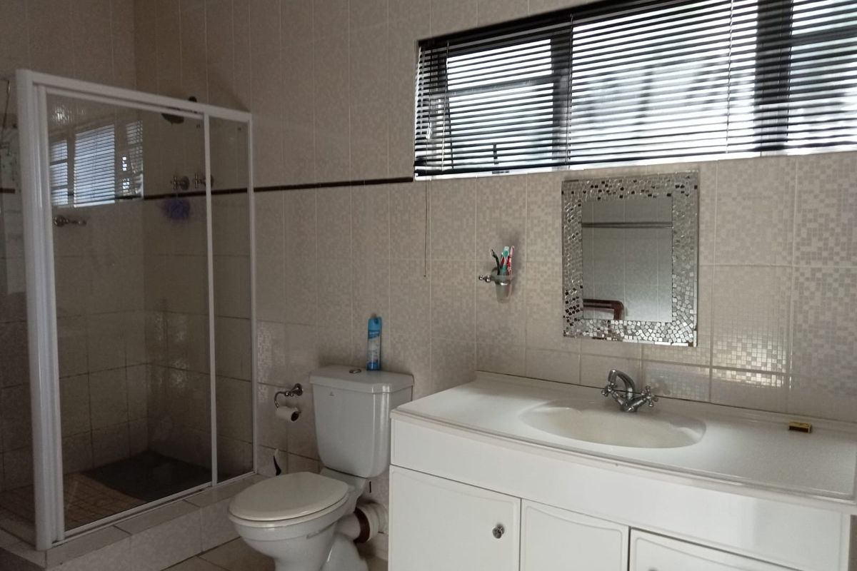 A functional bathroom featuring a glass-enclosed shower, a white vanity with integrated basin, and a standard toilet, finished with neutral wall tiles.